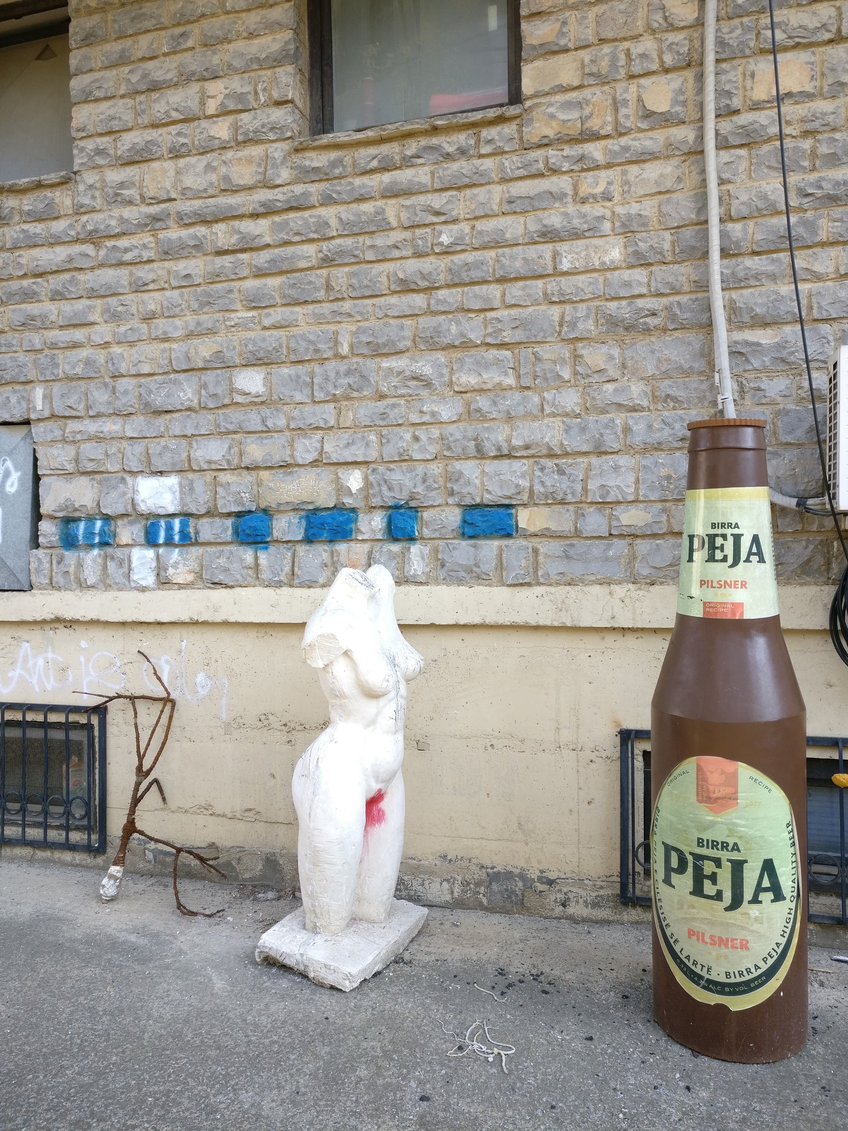 Patsas päättömästä naisesta ja oluesta. Kuva on otettu Pristinan ylipiston taideakatemian pihalta.